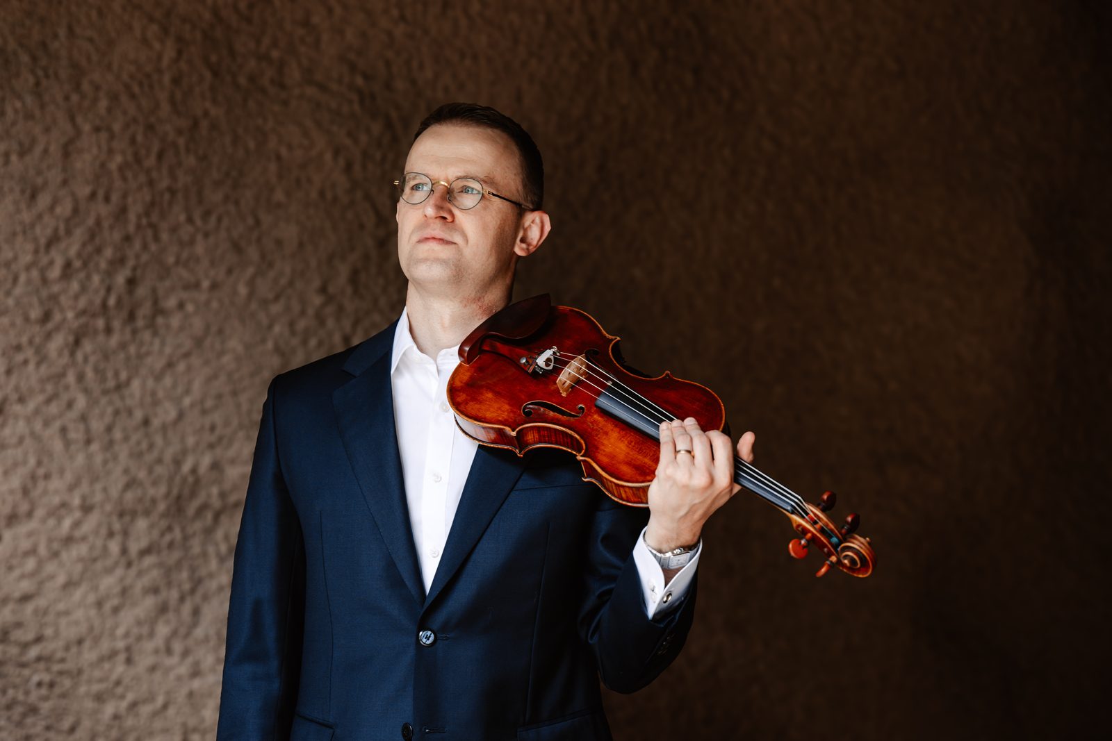 David Southorn crouching with violin and bow against a stone wall