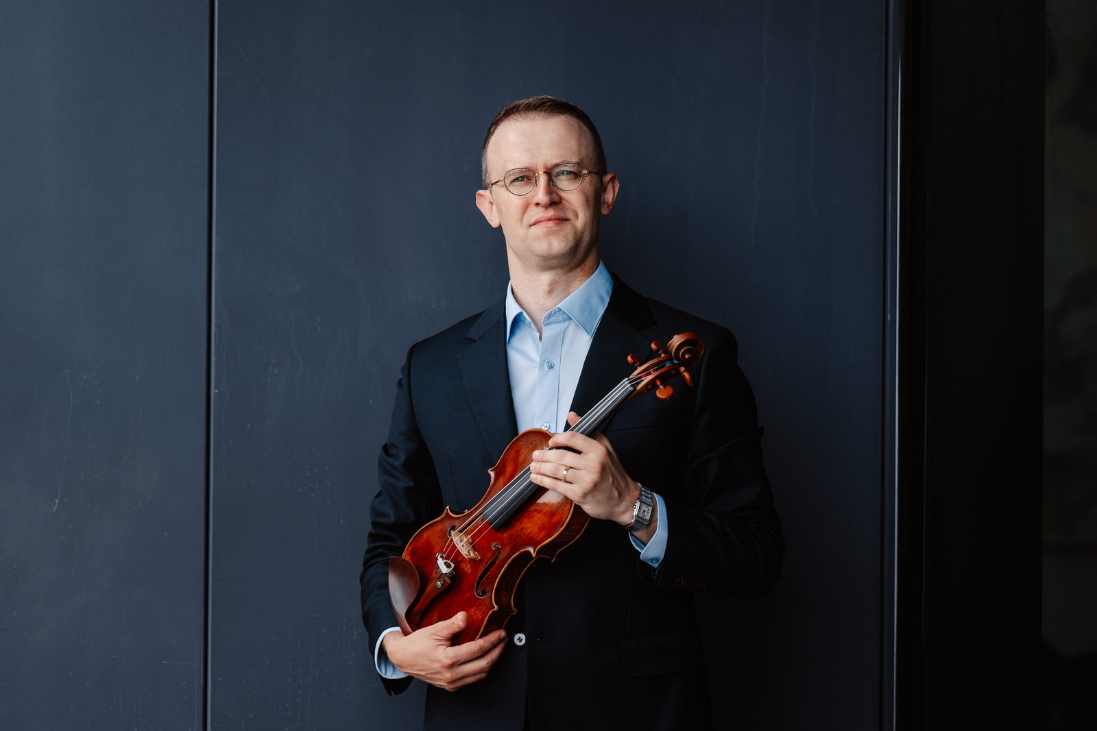 David Southorn holding his violin, dark wood panel background