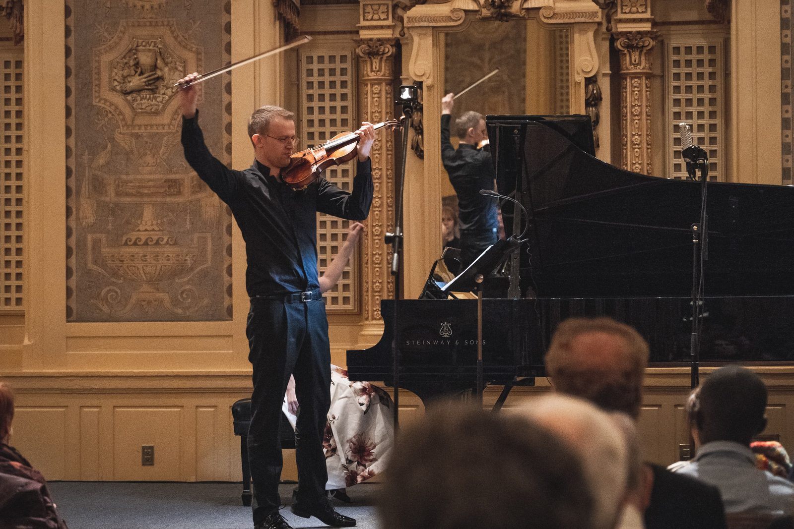David Southorn, full-length portrait in a dark suit with violin, grey wall