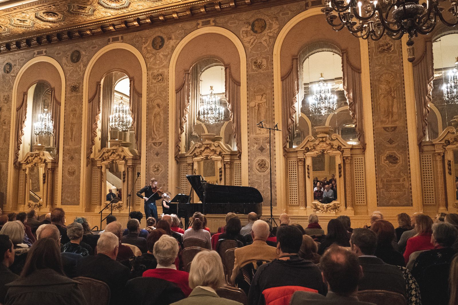 Wide view of a concert hall stage with grand piano and performers