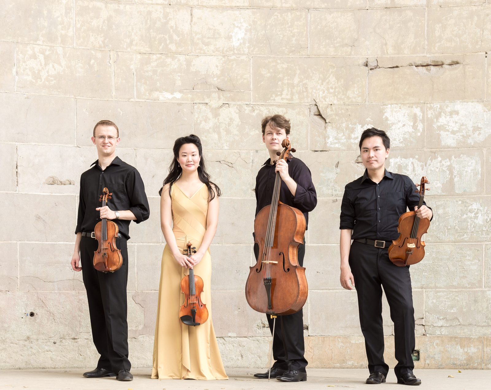 Four musicians, including David Southorn, standing against a light stone wall